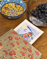 Folk-art bird postcard beside an ornate floral bowl and a bowl of blackberries