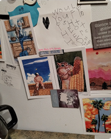 A fridge door covered with magnets and quirky art postcards including a winged cat