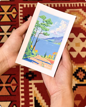 Vibrant postcard of a Mediterranean coastline and blue bay held against a kilim rug